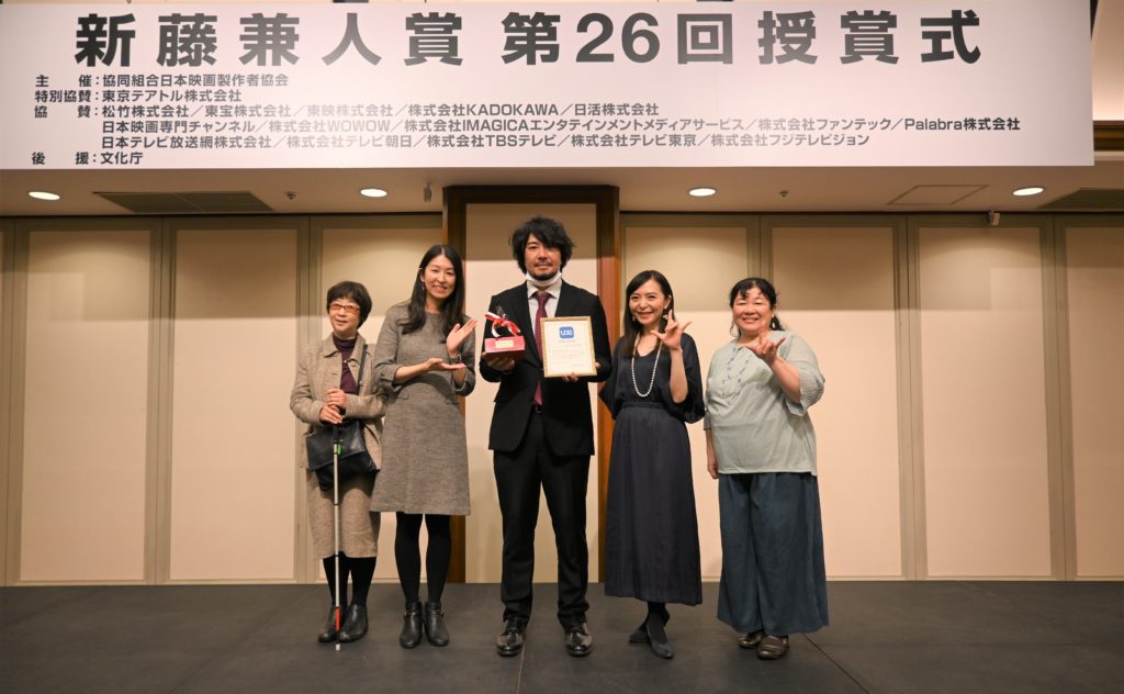 授賞式の壇上で記念写真。左から、音声ガイドユーザー、代表の山上、藤元監督、字幕ユーザーの二人で計５人。